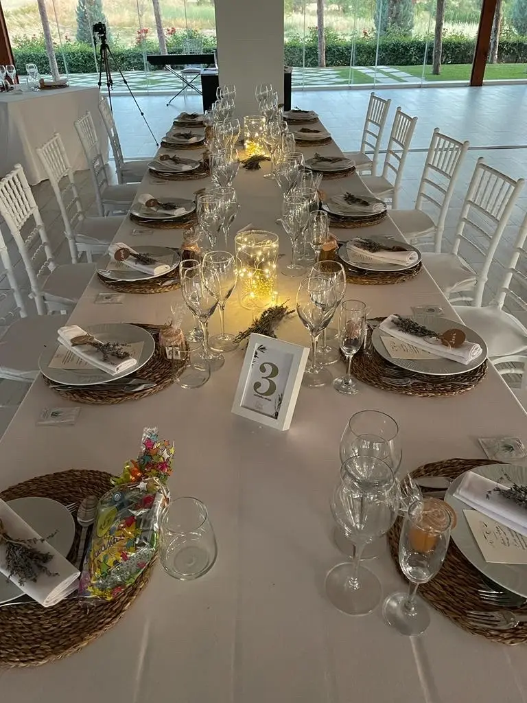Una mesa larga puesta con platos de mimbre, copas, velas y una tarjeta con el número 3